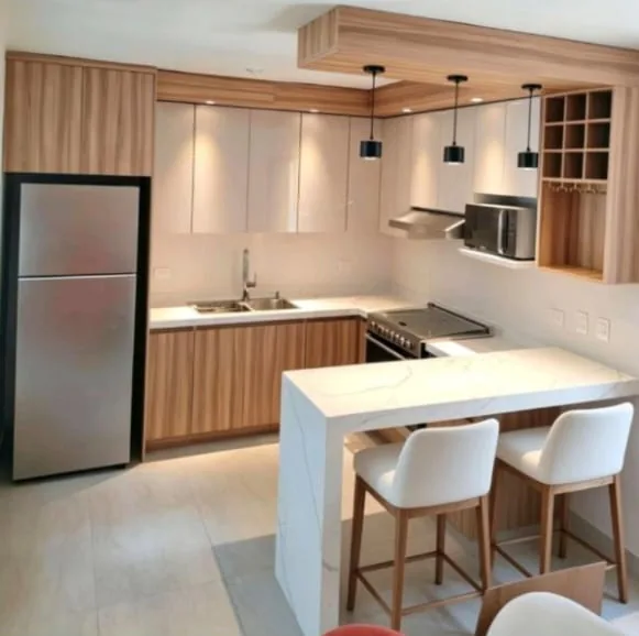 Obra real: cocina en L con barra de cuarzo, gabinetes en madera y lámparas colgantes