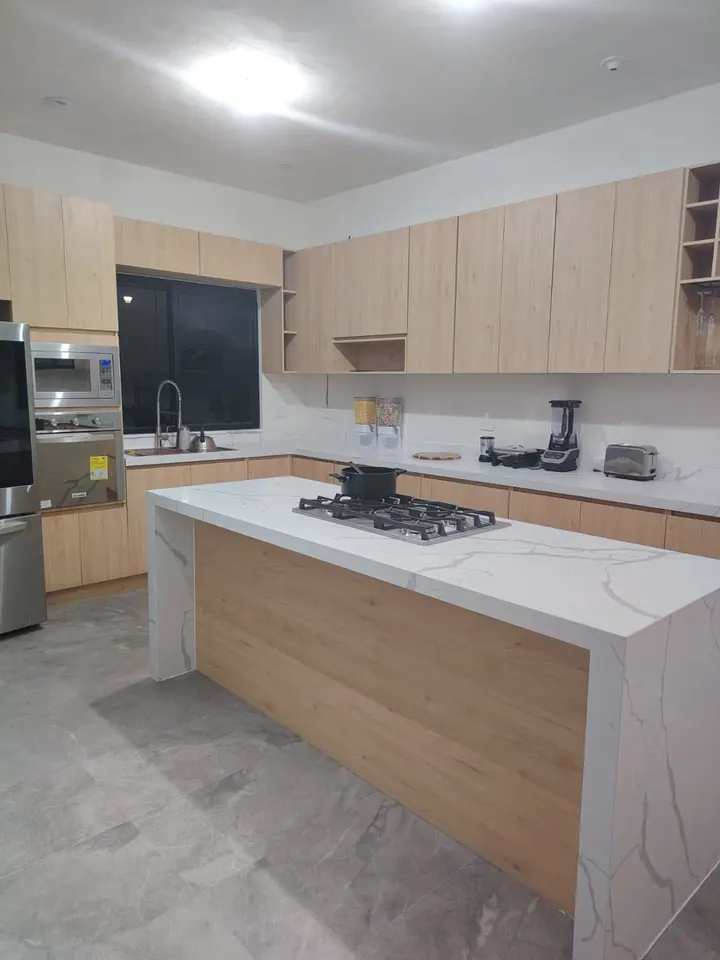 Obra real: cocina con isla de cuarzo en cascada, gabinetes en madera clara y campana